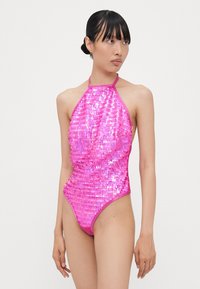 Maillot de bain rose pailleté avec un design à col halter, présentant une silhouette ajustée et un détail froncé sur le côté. Surface brillante et texturée.