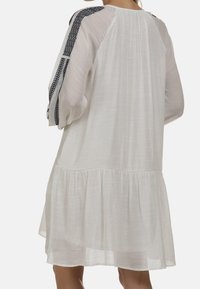 Biała sukienka z długimi, bufiastymi rękawami z czarnym haftem na ramionach. Zwiewny fason z marszczonym dołem. Lekki materiał.