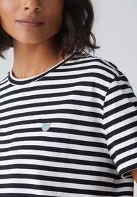 Zwart-wit gestreepte T-shirt met ronde hals en korte mouwen, met een klein blauw hartje geborduurd op de borst.