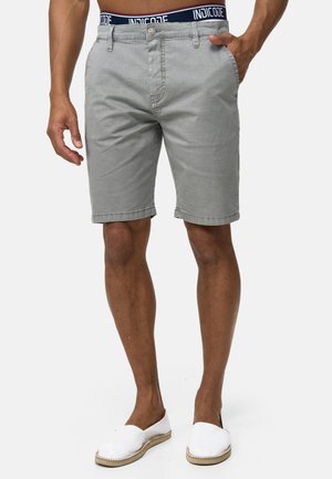 Shorts gris à motifs avec fermeture à bouton et à zip, dotés d'une taille bleu marine avec le logo "INDICODE" ; portés avec des chaussures blanches à enfiler.