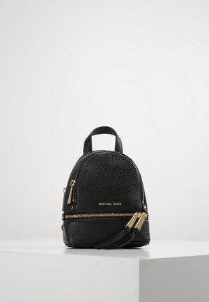 Zwart gestructureerd leren mini-rugzak met gouden ritsen en "Michael Kors"-logo aan de voorkant, geplaatst op een witte sokkel tegen een effen achtergrond.