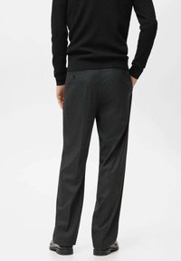 Dark gray tailored trousers with a straight fit, featuring two back pockets and a subtle check pattern. Worn with a black ribbed sweater.