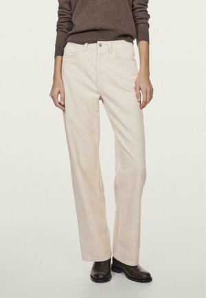 Jasno-beżowe spodnie z korduroy o prostym kroju, z widocznymi szwami i przednimi kieszeniami, zestawione z brązowym swetrem i czarnymi botkami.