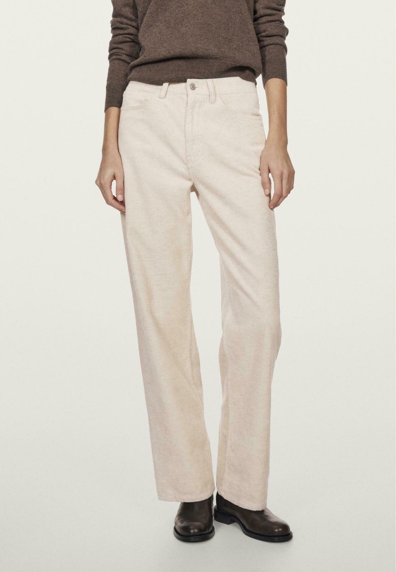 Lys beige kordfløjspant med et lige ben-design, synlige sømme og forlommer, parret med en brun trøje og sorte støvler.