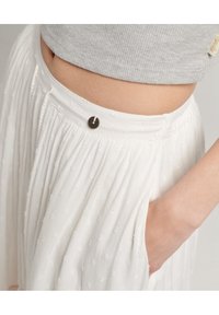 Witte, geplooide rok met gestructureerde patronen en een knoopsluiting, voorzien van zijzakken en gemaakt van een zacht, lichtgewicht materiaal.