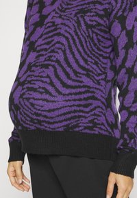 Sweter w czarno-fioletowy wzór zebry o strukturalnym dzianinie. Posiada ściągacze na dole i rękawach oraz luźny krój, który pomieści brzuszek.