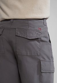 Graue Cargo-Shorts mit mehreren Seitentaschen, einer glatten Textur und einem kleinen gestickten Flaggenakzent. Das Material wirkt leicht und strapazierfähig.