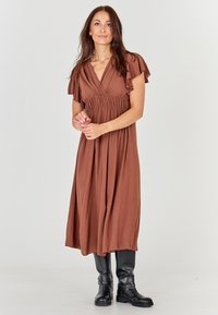 Brūnas, plūstošas maxidresses ar īsām volānveida piedurknēm un savāktu vidukli, kombinētas ar melniem potīšu zābakiem. Gluda auduma ar vieglu tekstūru.