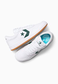 Sneaker in pelle bianca con una stella verde e un design a chevron. Presentano una suola in gomma naturale e una soletta interna blu con motivo. Con lacci e fori di ventilazione.