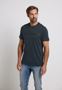 Tmavě modré tričko s krátkým rukávem z měkké bavlny, s výrazným černým grafickým potiskem s textem "HELD & STONE CO." na přední straně.