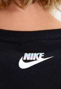 Close-up of a black shirt collar with a reflective Nike logo printed on the upper back below short blonde hair.