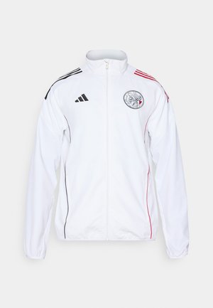Weißer Sportjacke mit schwarzen und roten Akzenten. Verfügt über einen durchgehenden Reißverschluss, hohen Kragen und Schulterstreifen. Vorderes Logodetail sichtbar.