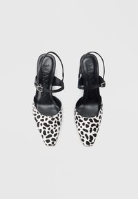 Pantofi slingback cu vârf ascuțit, având un imprimeu leopard alb-negru, cu o curea subțire reglabilă la gleznă și un interior neted negru.