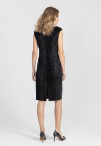 Czarna sukienka bez rękawów wykonana z teksturowanej tkaniny o delikatnym połysku, długości do kolan, z rozcięciem z tyłu dla swobody ruchów.