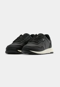 Μαύρα αθλητικά παπούτσια με λείο συνθετικό επάνω μέρος, υφασμάτι να διακοσμητικά στοιχεία, στρογγυλά κορδόνια και επενδεδυμένη εκρού σόλα. Διαθέτουν λογότυπο στη πλευρά.