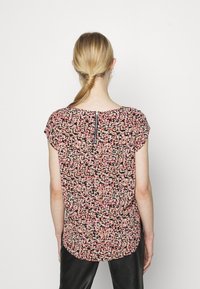 Blouse florale sur fond sombre avec des motifs roses, jaunes et blancs. Présente des manches courtes et un détail de fermeture éclair au dos.
