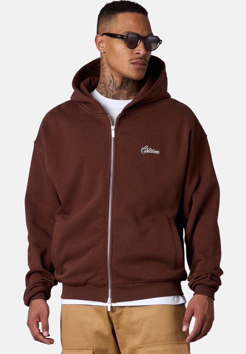 Brauner Zip-Hoodie mit einer großen Kapuze, gerippten Bündchen und einem elastischen Saum. Mit besticktem Branding auf der Brust und vorderen Taschen.