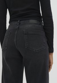 Black denim jeans with a high waist, straight leg, two back pockets, and a leather label on the waistband. Smooth texture, minimal fading.