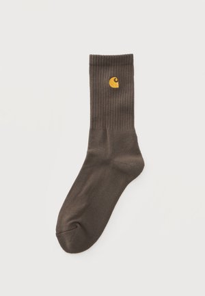 Single dark brown crew sock with ribbed cuff and small yellow logo near top on plain light background.