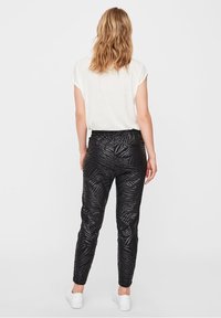 Czarne spodnie w zebrę o gładkiej fakturze, dopasowane, z elastycznym paskiem w talii, połączone z luźną białą bluzką.