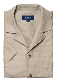 Camicia beige con texture, colletto classico, tre bottoni in legno marrone e una piccola tasca sul petto. Etichetta Eton visibile sul colletto.