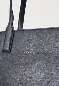 Sötétkék, textúrált bőrtáska dupla pánttal, az elején arany színű 'TOMMY HILFIGER' logóval. Simább felület, minimalista dizájn.
