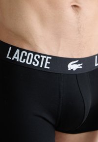 Boxers en coton noirs au design ajusté, avec une large ceinture élastique imprimée "LACOSTE" en blanc et un logo de crocodile.