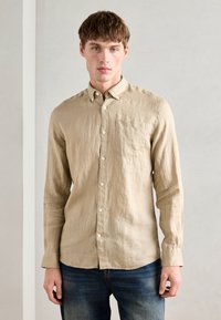 Camisa bege de mangas longas, com botões, feita de linho leve; possui um bolso no peito, botões brancos e um corte casual com a barra reta.