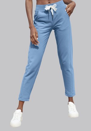 Blue sweatpants in soft fabric feature a drawstring waist, side pockets, and tapered legs, paired with white sneakers.