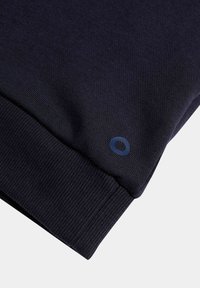 Pulóver de un oscuro azul marino con una textura suave, puños acanalados y un pequeño logo redondo en azul en la manga.