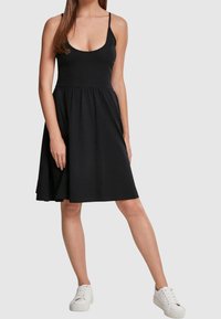 Svart ärmlös klänning med rundad halsringning och samlad midja, som flyter ut i en knälång kjol. Matchas med vita sneakers.