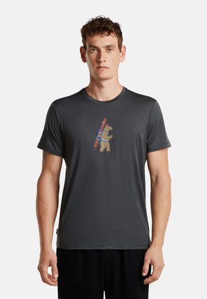 Mann trägt ein dunkelgraues T-Shirt mit einer Grafik eines Bären, der Skier und Wanderstöcke vorne trägt.