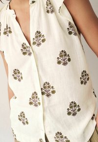 Biała lniana bluzka z krótkimi rękawami, ozdobiona misterną brązowo-zieloną kwiatową haftą, zapinana na guziki z przodu, o luźnym kroju.