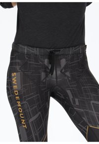 Black activewear leggings featuring a geometric gray pattern, drawstring waist, and "SWEDEMOUNT" logo in gold. Textured waistband.