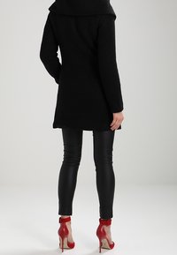 Black textured coat with a wide collar, paired with black leather leggings and red ankle strap heels. Focus on composition and fit from the back.
