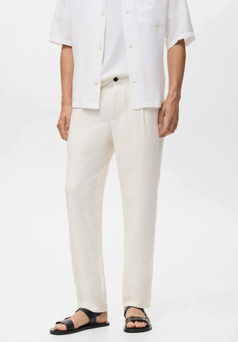 Pantaloni di lino color crema con un design a gamba dritta, abbinati a una camicia bianca a maniche corte e sandali neri. Stile minimalista.