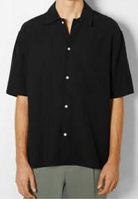 Czarna koszula z krótkim rękawem, zapinana na guziki z przodu, białe guziki, kołnierz typu rozpiętego oraz kieszeń na lewej piersi, wykonana z gładkiej tkaniny.