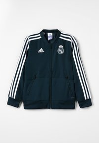 Marinenblå Adidas-jakke med hvide striber på ærmerne, fuld frontlynlås, to lynlåsede lommer og Real Madrid-logo på brystet.