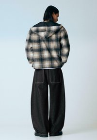 Bézs, fekete és szürke kockás, túlméretezett dzseki kapucnival; laza sötét farmernadrággal, melyen hátul zsebek találhatók.