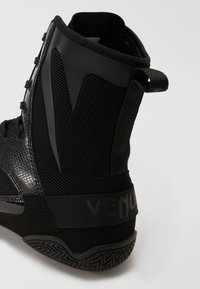 Stivale sportivo nero con tomaia in mesh testurizzato e sintetico liscio, supporto per la caviglia e una suola in gomma con grip a motivi.