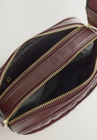 Donkerbruin gequilte leren tas met twee open hoofdcompartimenten, die de zwarte stoffen voering en de goudkleurige ritsen laat zien.