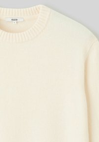 Pull crème avec un col rond côtelé et une texture lisse. Fabriqué à partir d'un matériau doux et léger. L'étiquette indique "B BZB" et la taille "L."