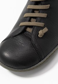 Černá kožená bota se zaoblenou špičkou, hnědými tkaničkami a ozdobným prošíváním. Podešev má decentní šedý vzhled.