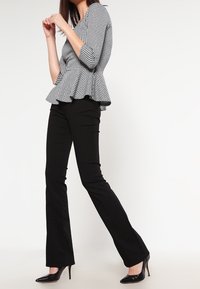 Black peplum top with a houndstooth pattern, three-quarter sleeves, paired with black flared pants and black high-heeled shoes.