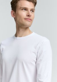 Hvid langærmet t-shirt lavet af blødt stof, med en rund hals og glat tekstur, som har minimal detaljer og en tætsiddende silhuet.