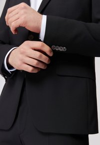 Giacca nera in tessuto liscio, con chiusura a un bottone, quattro bottoni sul polsino e design con rever a punta.