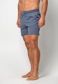 Shorts de bain gris avec une taille élastique, fermeture à cordon de serrage et poches latérales. Texture lisse, longueur au-dessus du genou et coupe décontractée.