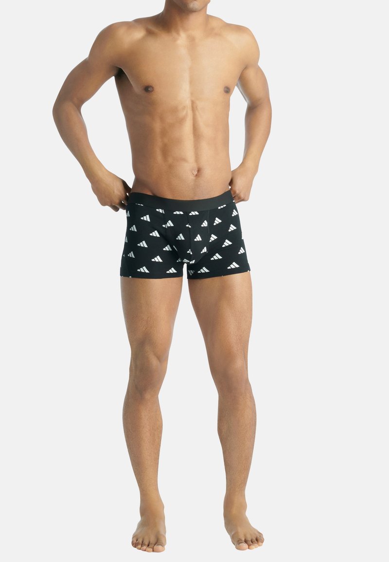 Svarta kalsonger med vita trekantiga mönster, elastiskt midjeband och en åtsittande design. Bärs av en person med bara fötter.