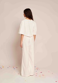 Macacão branco texturizado com mangas bufantes e um corte descontraído. Os detalhes incluem um tecido estampado e um design de pernas largas, com poucos acentos.