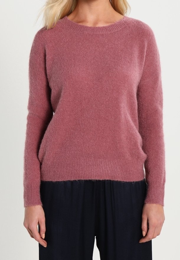 Maglione rosa lavorato a maglia con una texture morbida e soffice, scollo rotondo e maniche lunghe, abbinato a pantaloni scuri e fluidi.